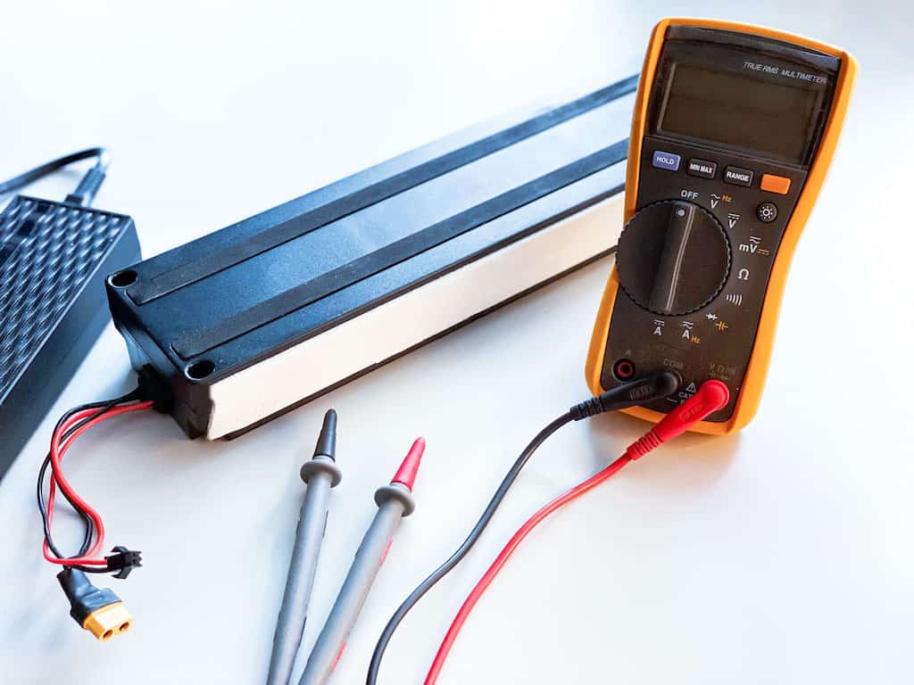 Akku Reparatur - ein E-Scooter Akku mit einem Multimeter und einem Ladegerät